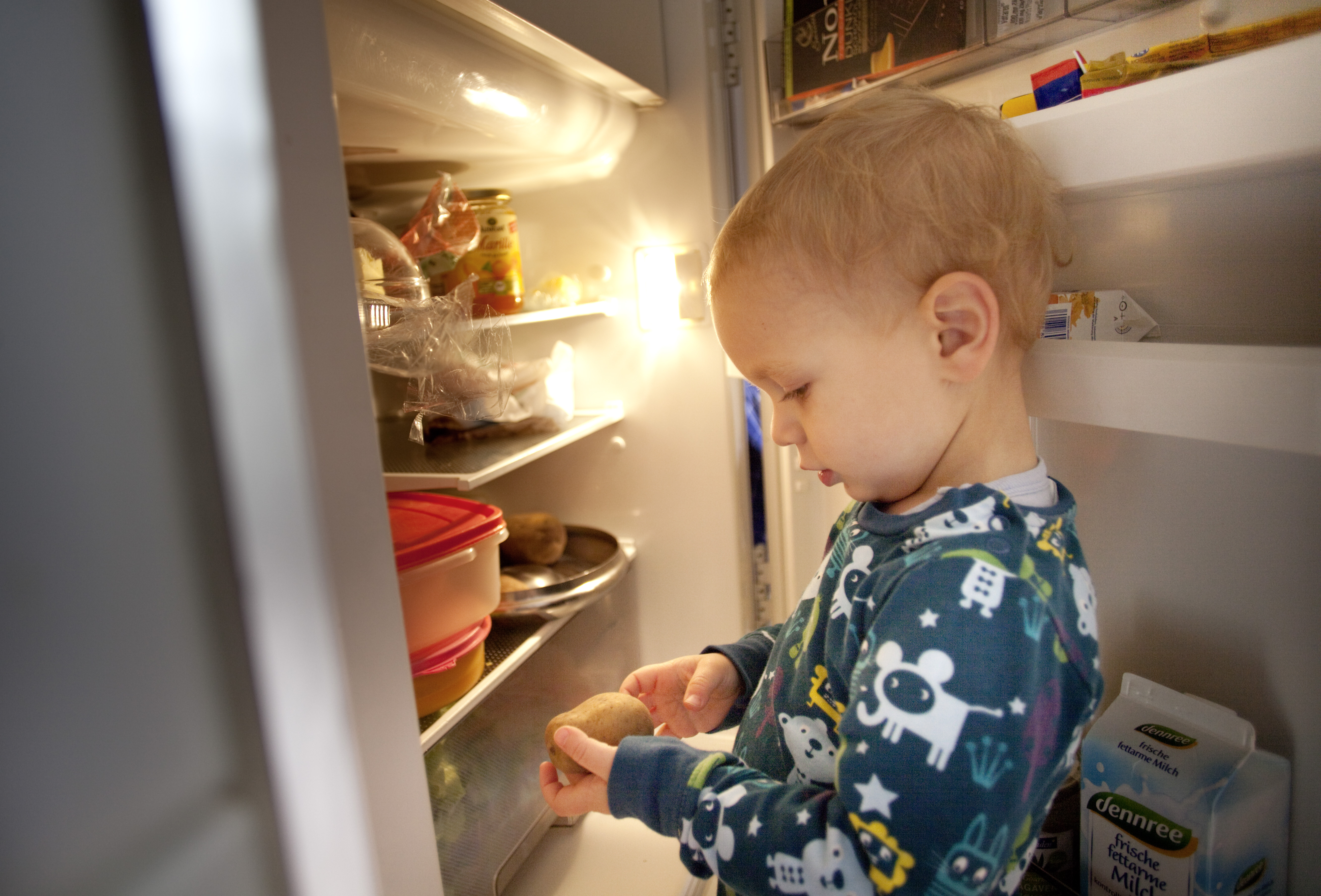 Kleines Kind guckt in den Kuehlschrank.