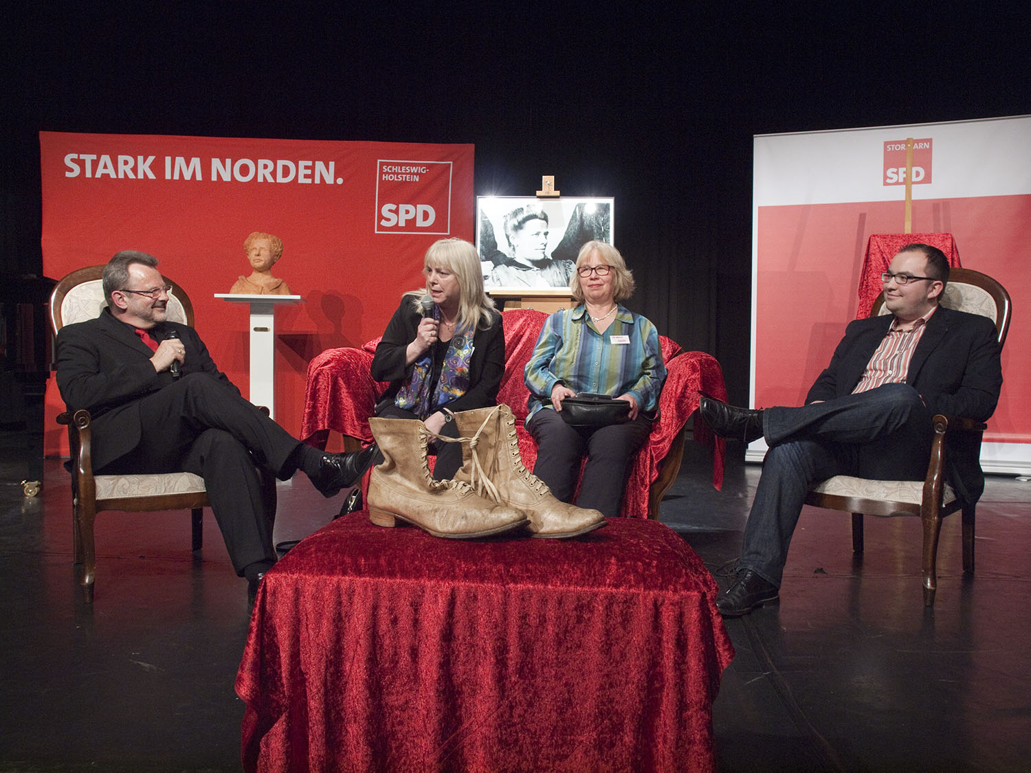 Gesprächsrunde mit Stiefeln von Louise Zietz: (v. l.) Moderator Franz Thönnes (MdB), Marina Spillner (Politikwissenschaftlerin), Susanne Schütt (Urgroßnichte), Sebastian Schütt (Ururgroßneffe).