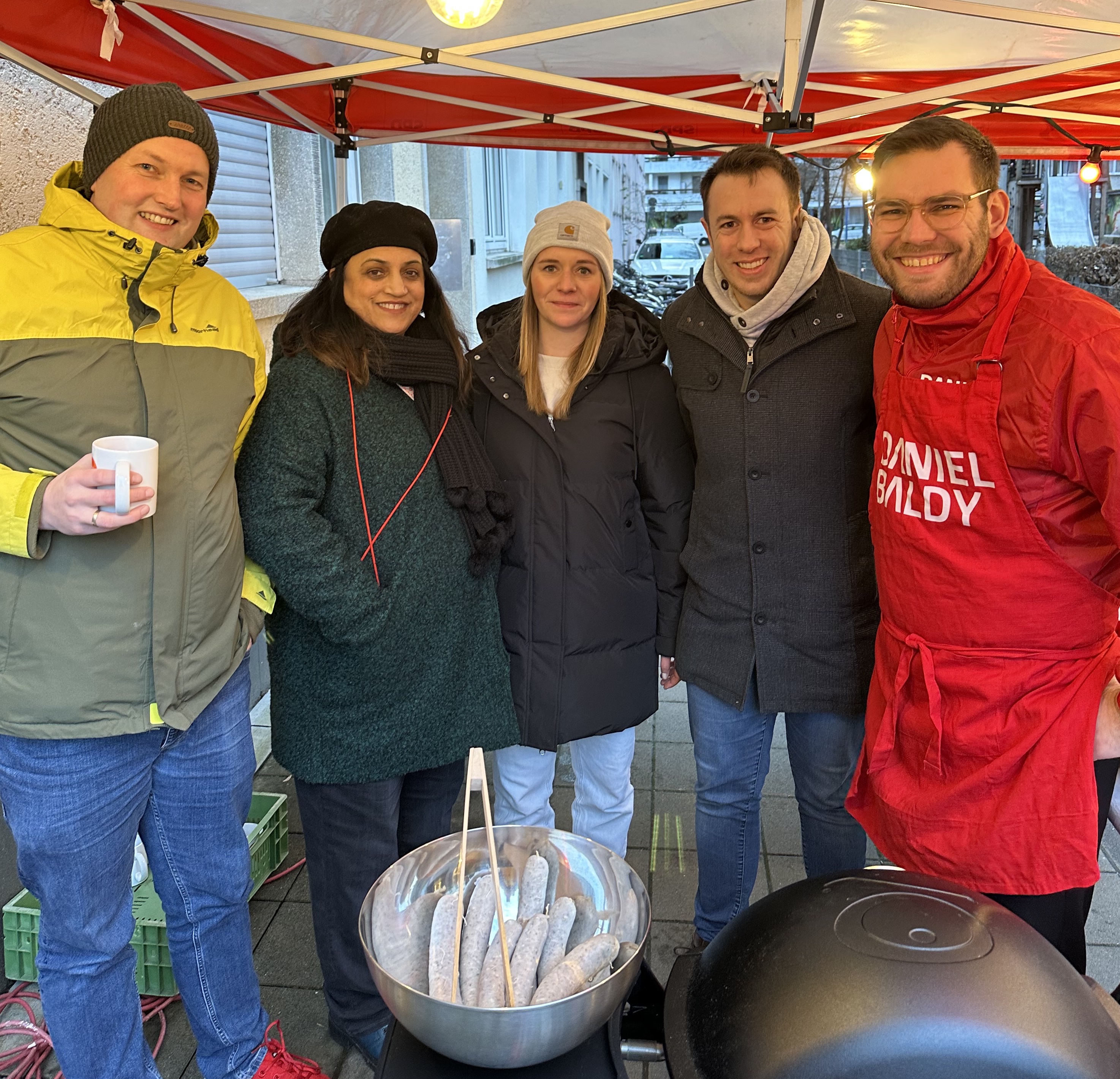 „Baldy brutzelt“: Der Bundestagsabgeordnete Daniel Baldy (rechts), steht in Mainz am Grill und kommt bei einer Bratwurst mit den Menschen ins Gespräch.