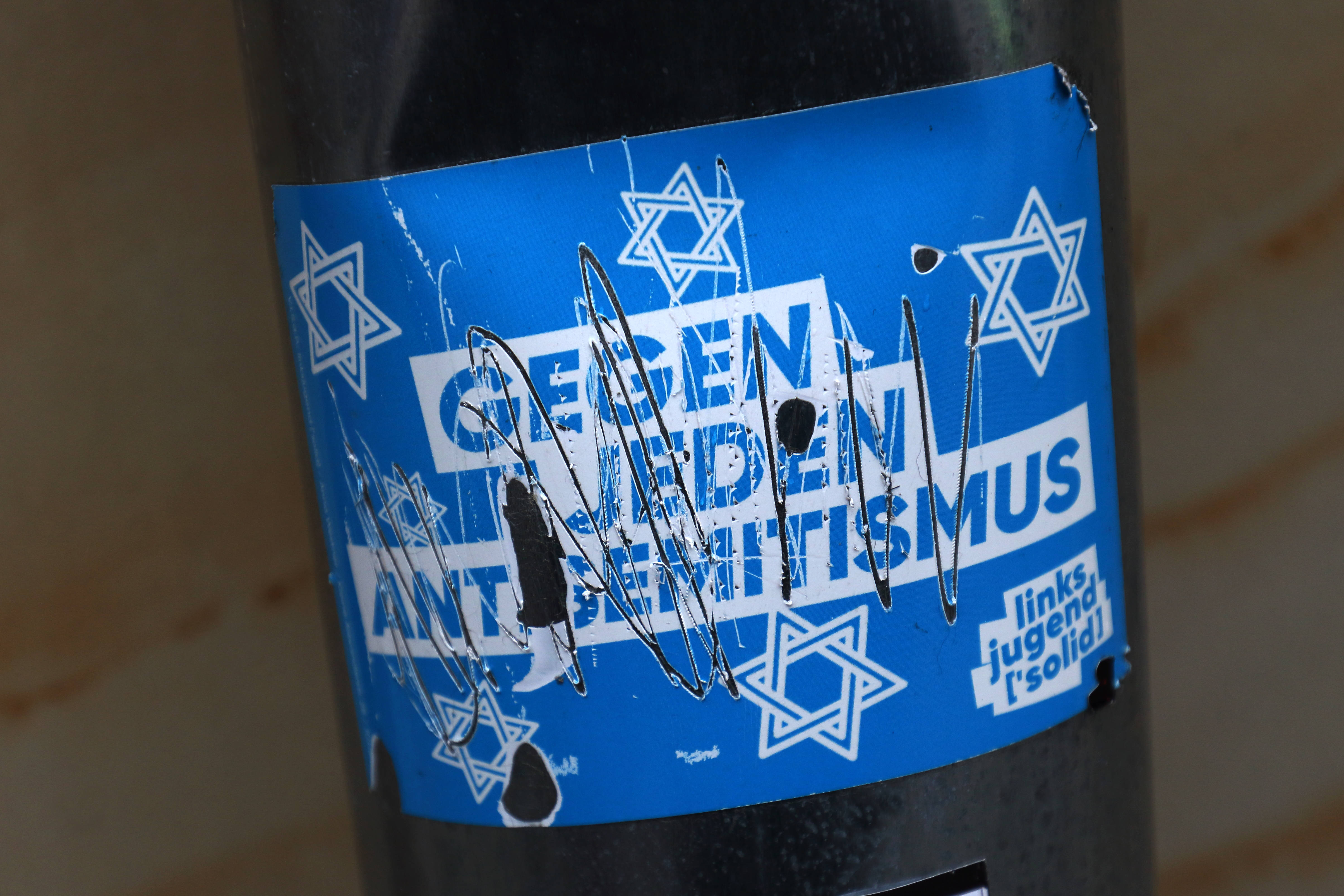 Ein Sticker mit der Aufschrift „Gegen jeden Antisemitismus" wurde durchgekratzt.