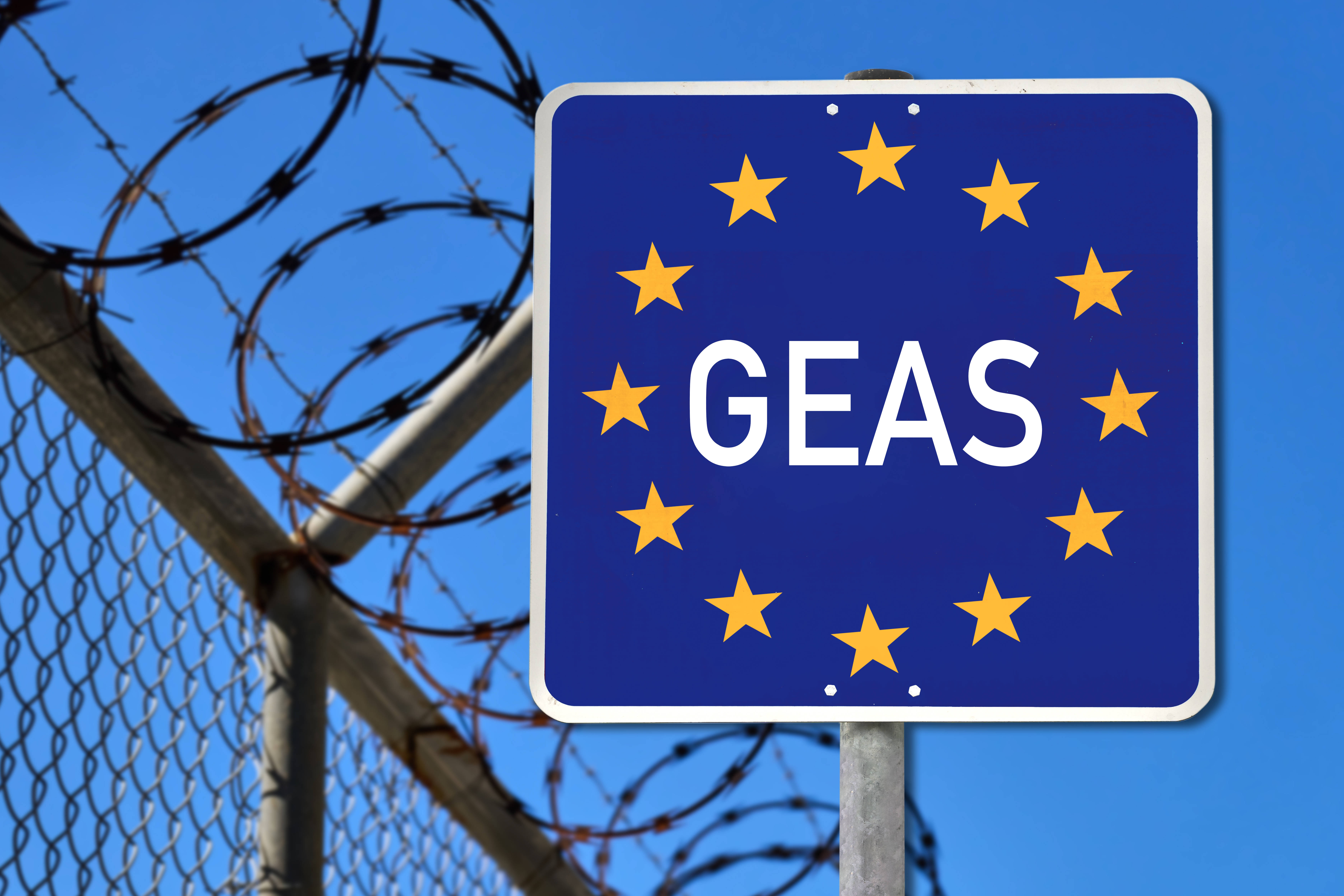 Fotomontage Grenzzaun mit Schild, auf dem GEAS (Gemeinsames Europäisches Asylsystem) geschrieben steht und die zwölf Sterne abgebildet sind, die die Europäische Union symbolisieren