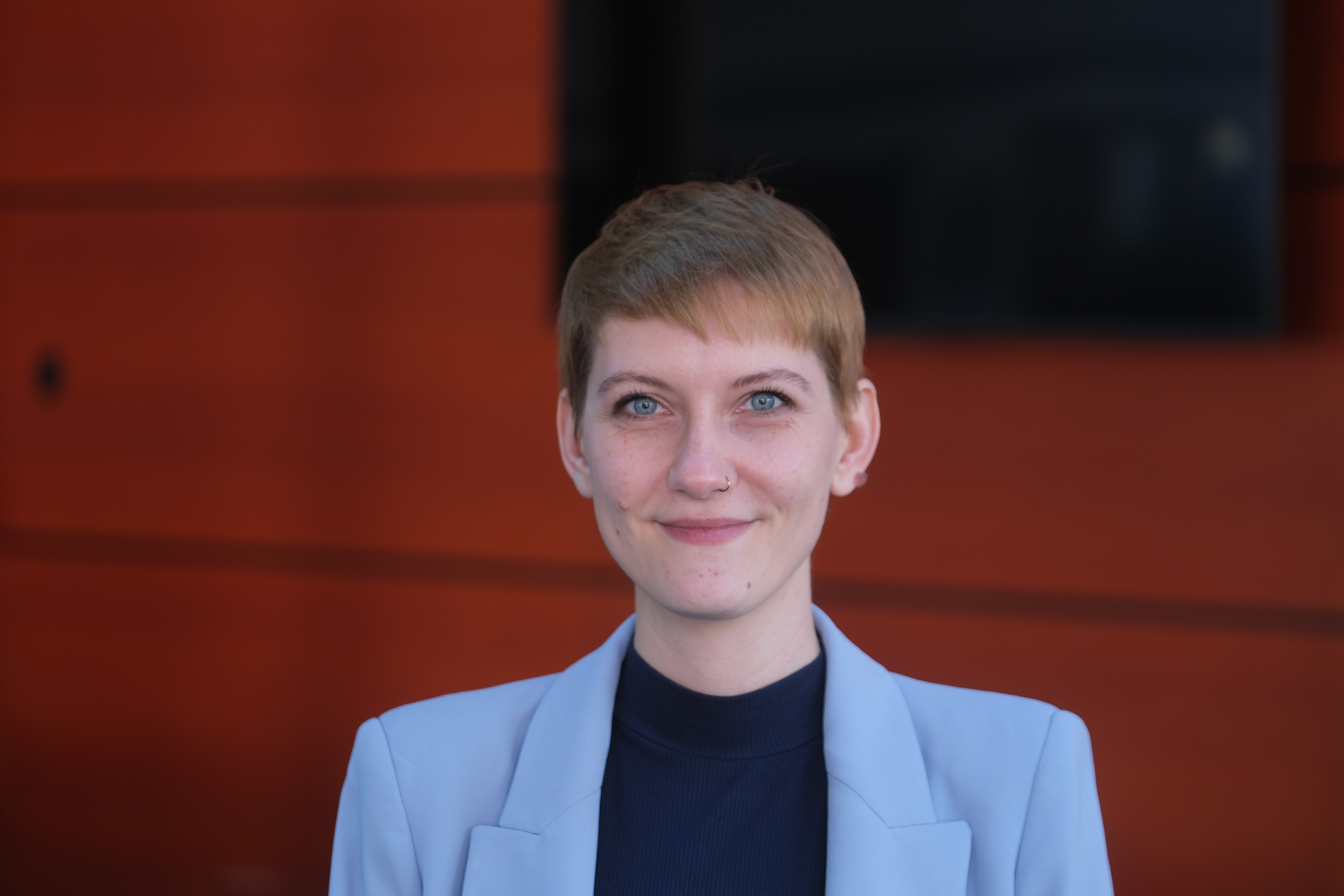 Neue Queer-Beauftragte der Bundesregierung Sophie Koch im lila Sacko vor rotem Hintergrund