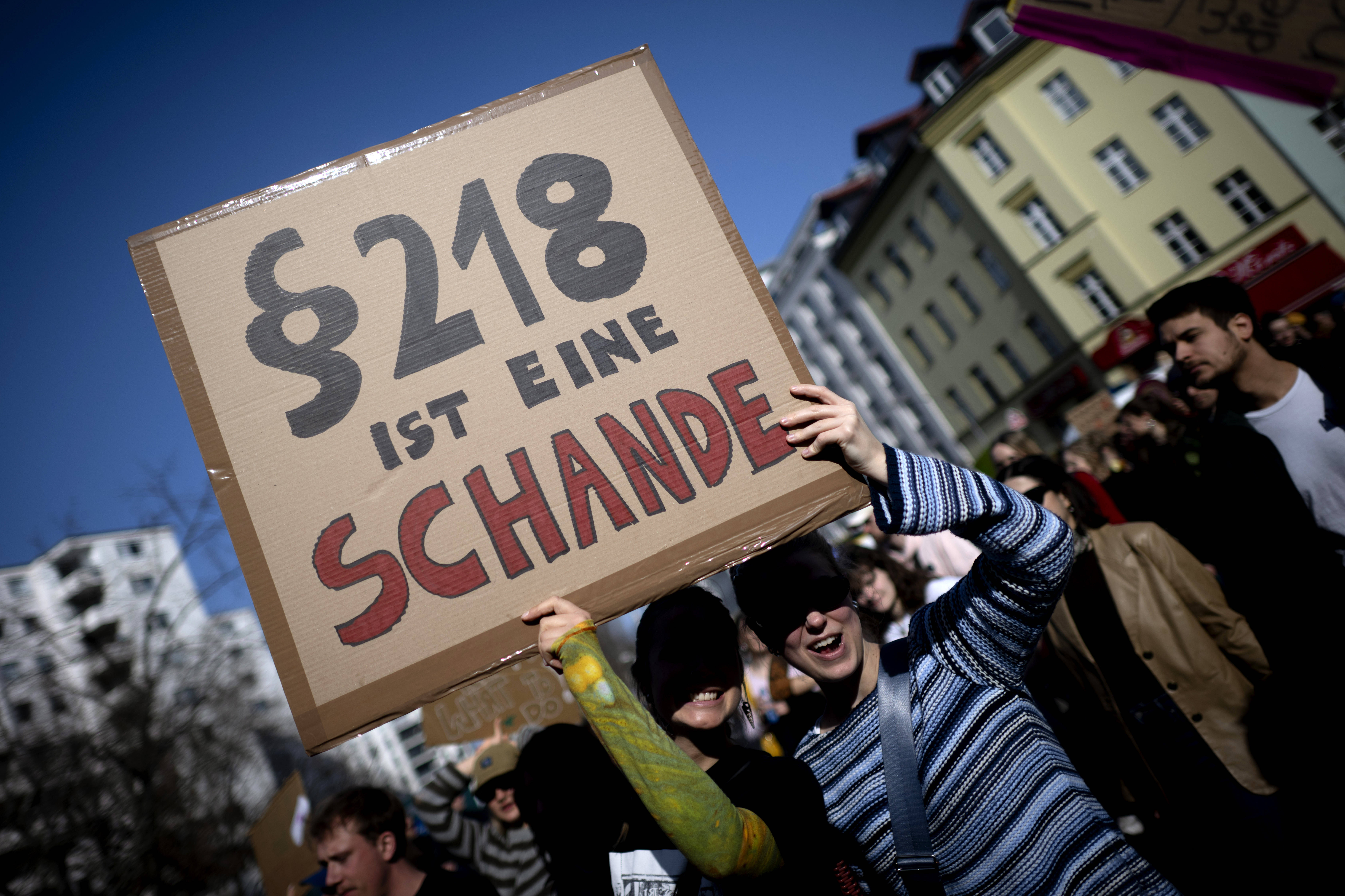 Menschen auf einer Demonstration mit einem Schild, das die Aufschrift „Paragraph 218 ist eine Schande“ trägt