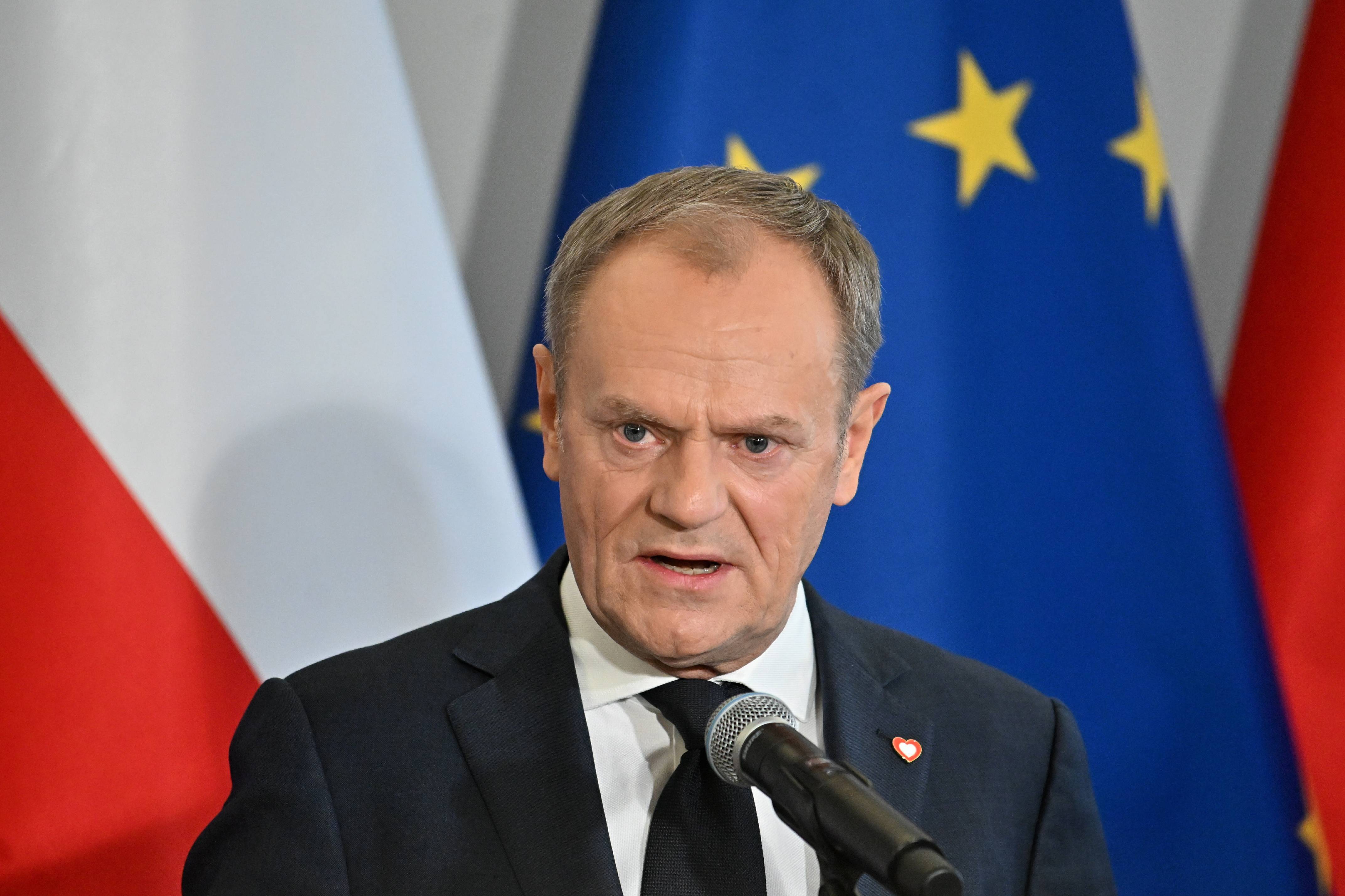 Polens Ministerpräsident Donald Tusk spricht in ein Mikrofon vor einer polnischen und einer EU-Fahne.