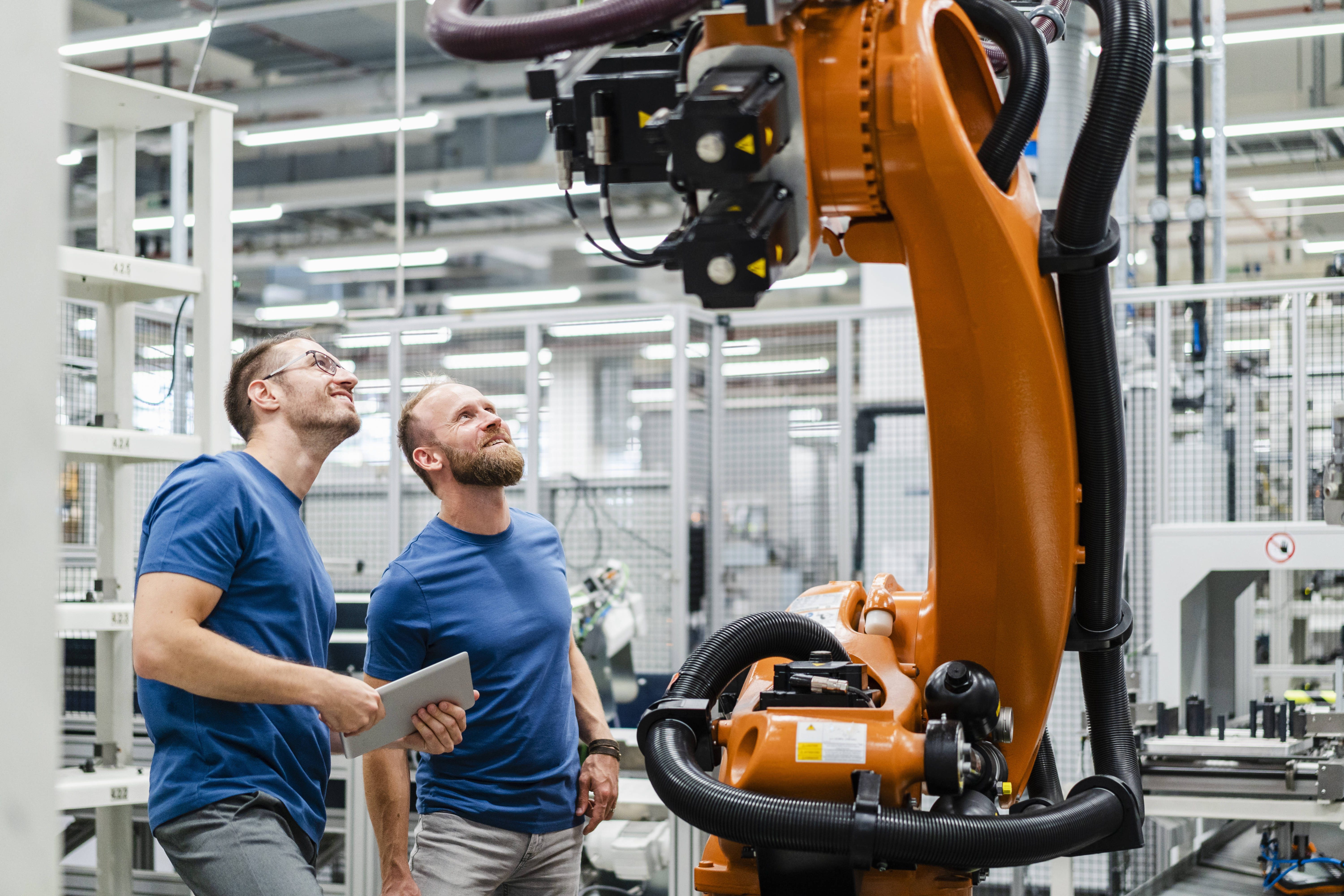 Zwei Männer in blauen T-Shirts vor einem Fertigungsroboter in einer Fabrik