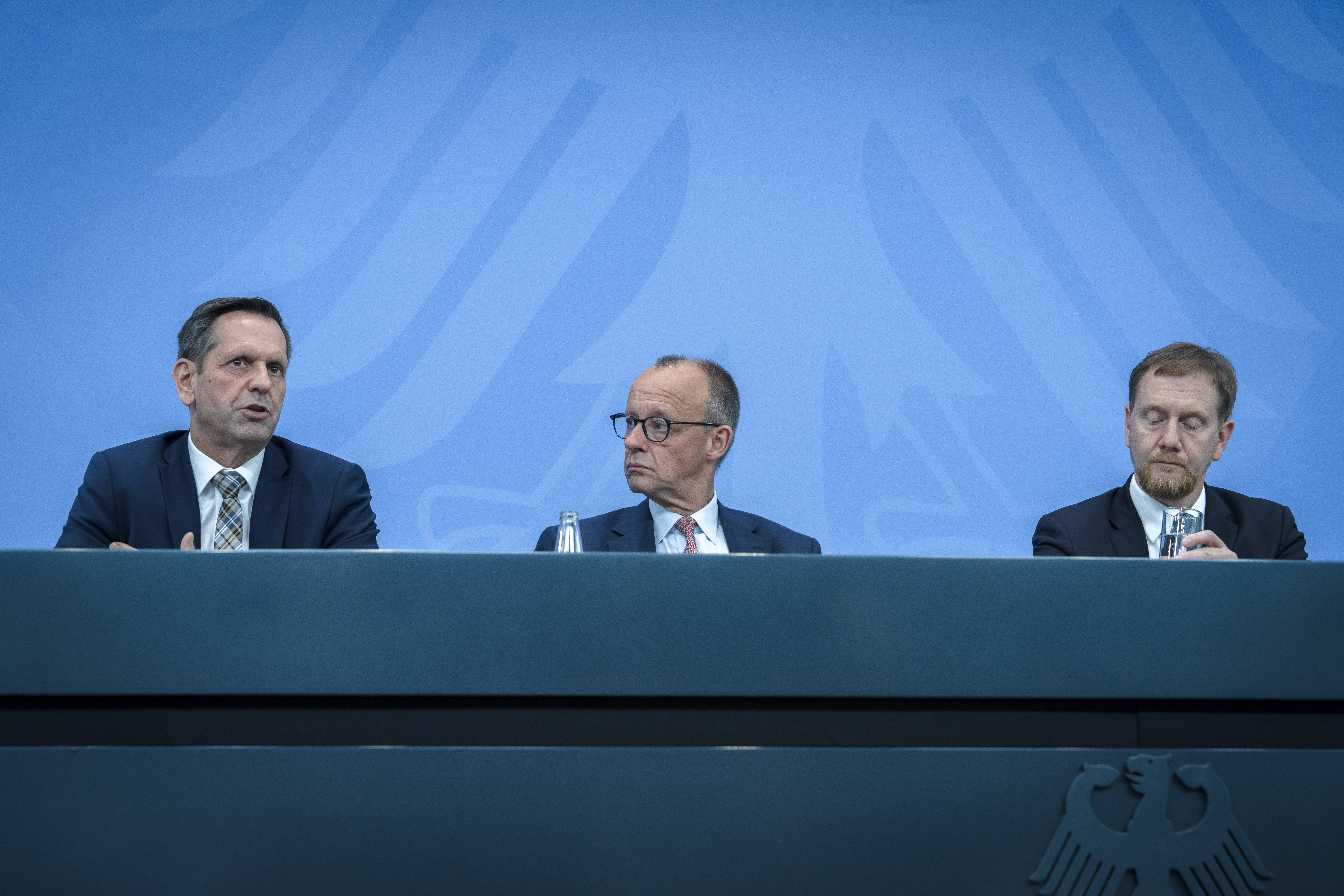 Olaf Lies, Friedrich Merz und Michael Kretschmer bei einer Pressekonferenz vor einer blauen Wand mit Bundesadler