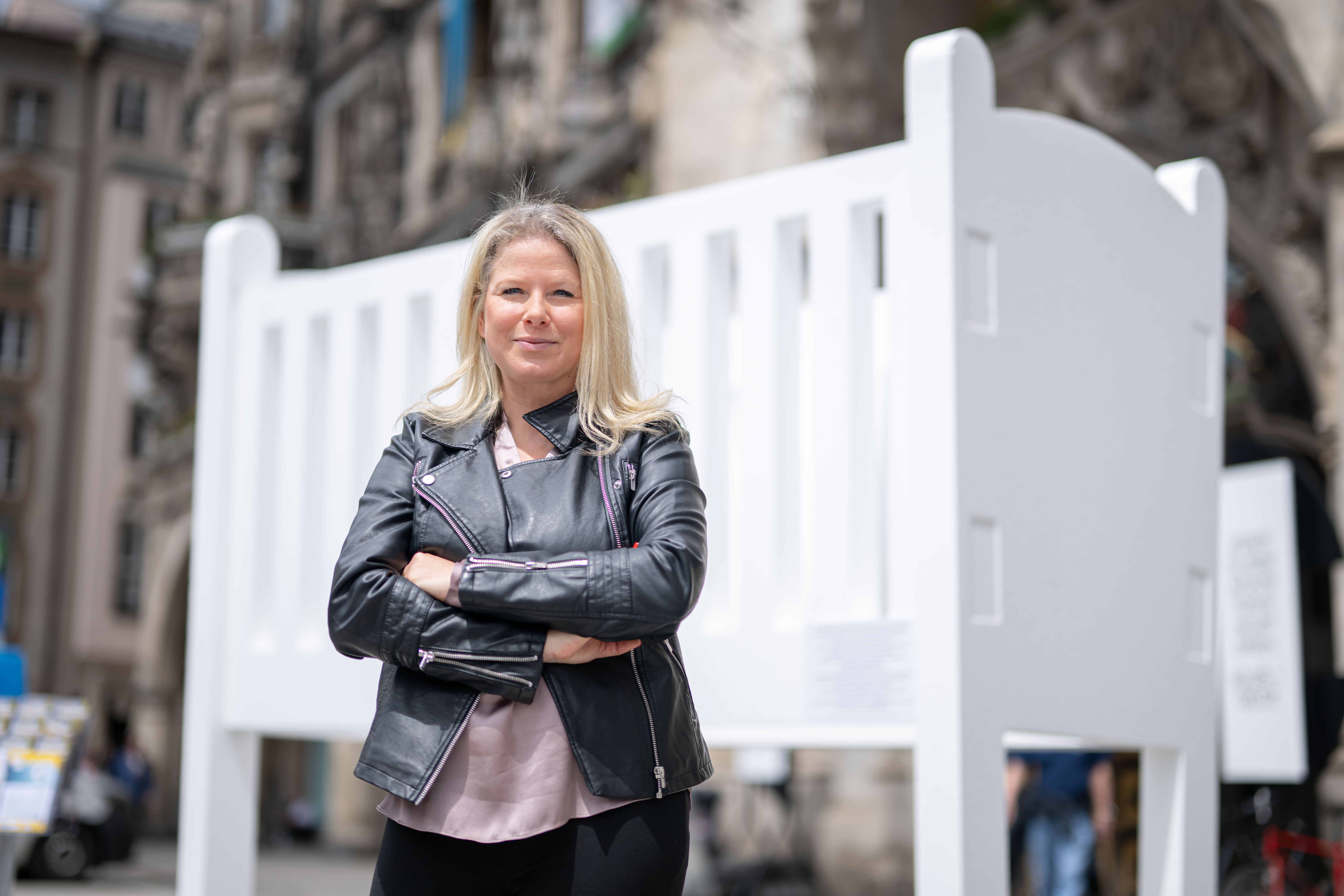 Natascha Sagorski steht mit verschränkten Armen in einer schwarzen Lederjacke vor einer zweieinhalb Meter hohen leeren Krippe auf dem Marienplatz in München.