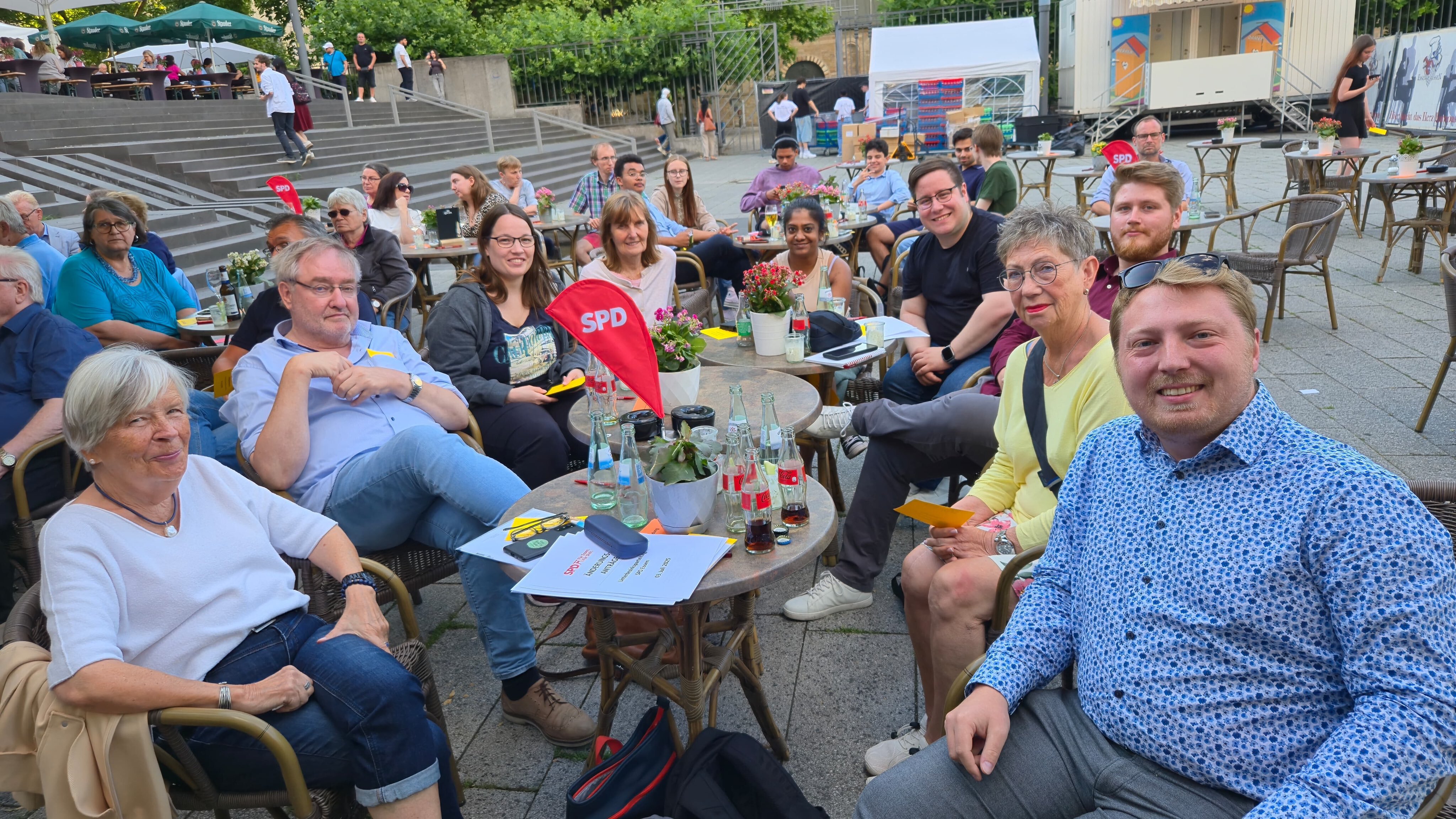 Viele Menschen sitzen auf einem Platz um kleine Tische herum.