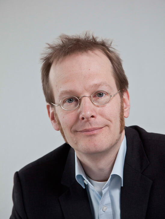 Ein lächelnder Mann mit roten Haaren und Anzug.