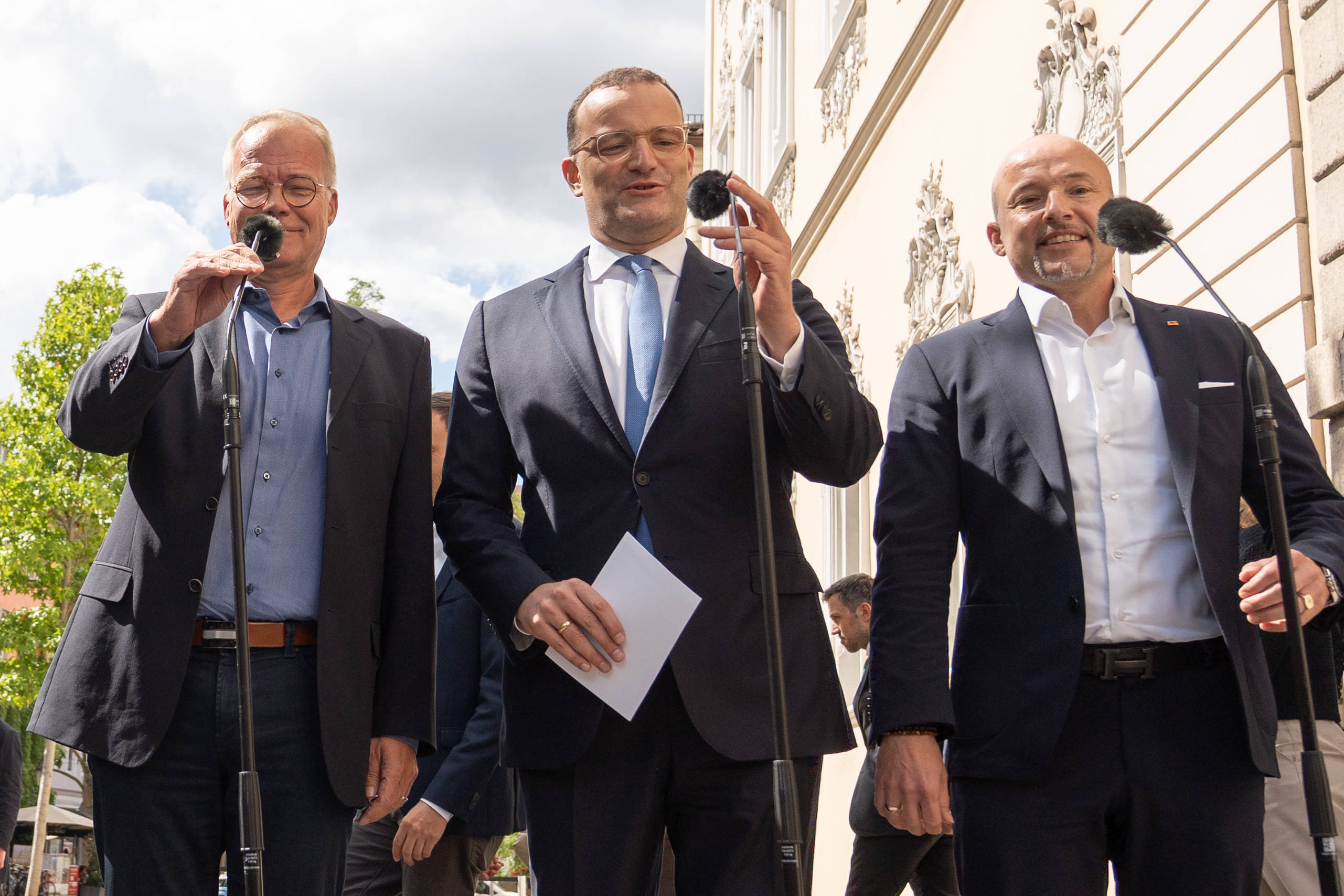 Matthias Miersch, Jens Spahn und Alexander Hoffmann stehen bei gutem Wetter draußen vor Mikrofonen.