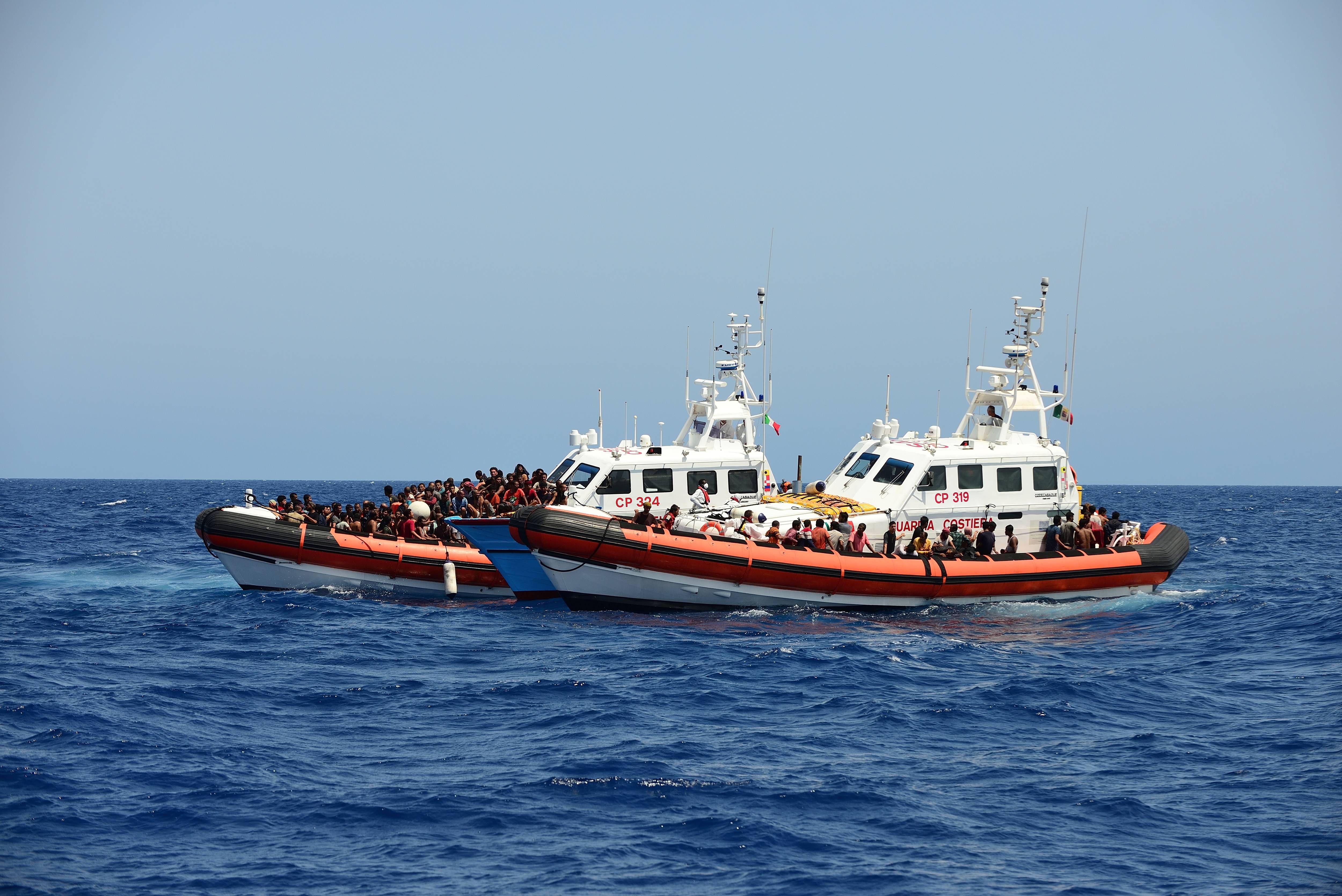 Schiffe der Italienischen Küstenwache evakuieren ein Boot mit Flüchtenden im Mittelmeer.