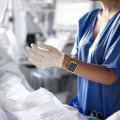 Eine Krankenschwester zieht sich einen Plastikhandschuh über.