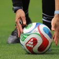 Ein Fußball liegt auf Rasen und wird von den Händen eines Schiedsrichters berührt.