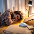 Eine junge Frau sitzt am Schreibtisch und legt erschöpft den Kopf auf den Tisch.